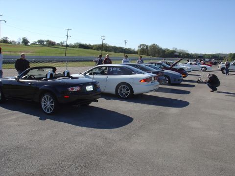 1993 Ford Probe - A line of cars are parked on a paved surface, with a white coupe in the foreground displaying racing numbers.
