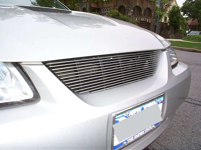 Front of a silver car with a horizontal chrome grille and a license plate