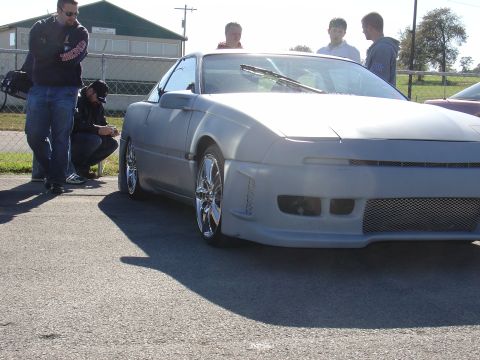 1993 Ford Probe - A gray car with custom modifications sits on asphalt under a bright sky.