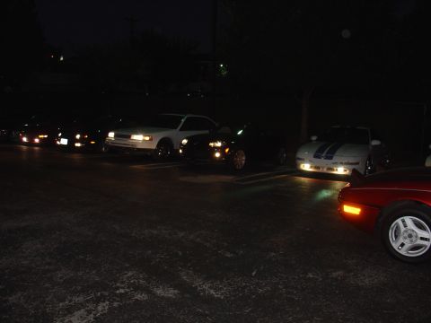 1993 Ford Probe - Several cars are parked in a lot at night, including a 1993 Ford Probe with racing stripes.