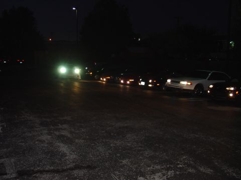 1993 Ford Probe - A group of vehicles are lined up in a parking lot after dark, with some headlights illuminated.