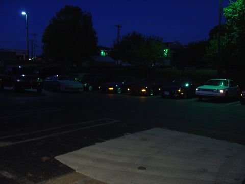 1993 Ford Probe - A collection of vehicles are parked in a lot after dark, illuminated by streetlights and building lights.