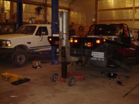 1992 Ford Bronco - Two trucks are parked inside a garage, one on a lift and the other with a flatbed.
