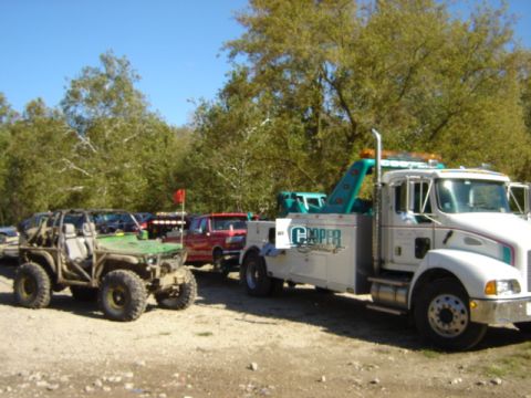1992 Ford Bronco - A tow truck is parked next to a modified off-road vehicle under a clear blue sky.