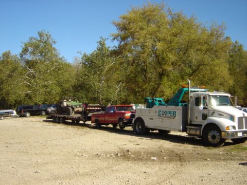 1992 Ford Bronco - Cooper Towing truck hauls a trailer loaded with a red pickup and a green off-road vehicle.