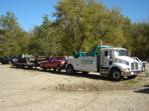 1992 Ford Bronco - A tow truck is transporting a trailer carrying a red pickup truck and a green ATV.