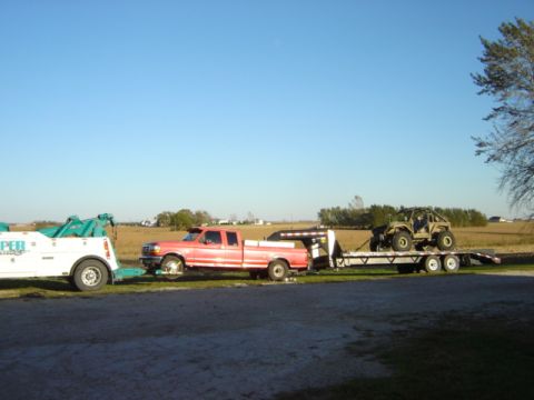 1992 Ford Bronco - A red pickup truck tows a trailer carrying an ATV across a field under a clear blue sky.