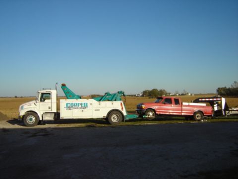1992 Ford Bronco - A white tow truck transports a red 1992 Ford F-250 pickup truck, which is hitched to a trailer.