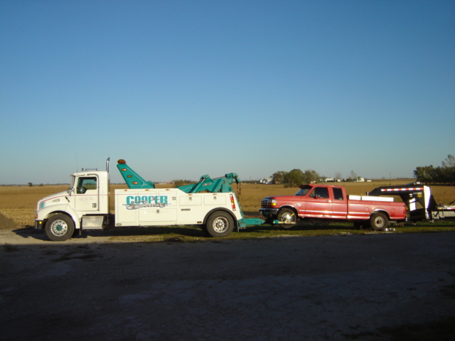Side view of a red 1992 Ford F-250 pickup truck being towed by a white tow truck