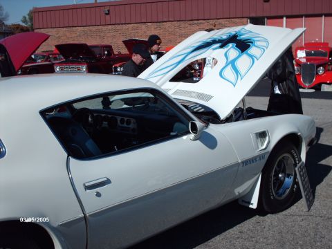 1995 Ford Probe - A white 1977 Pontiac Firebird Trans Am is displayed with its hood open, revealing a flame decal, at an outdoor car show.