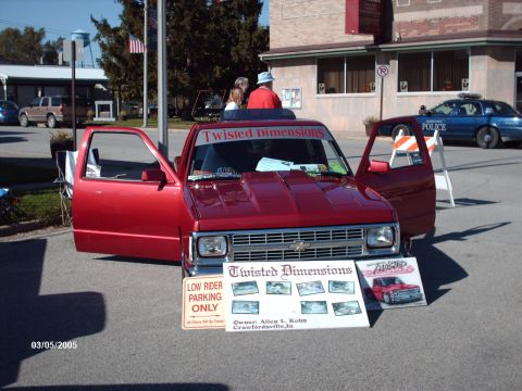 1995 Ford Probe - A red pickup truck with its doors open is displayed at a car show, with a "Twisted Dimensions" banner on the windshield.
