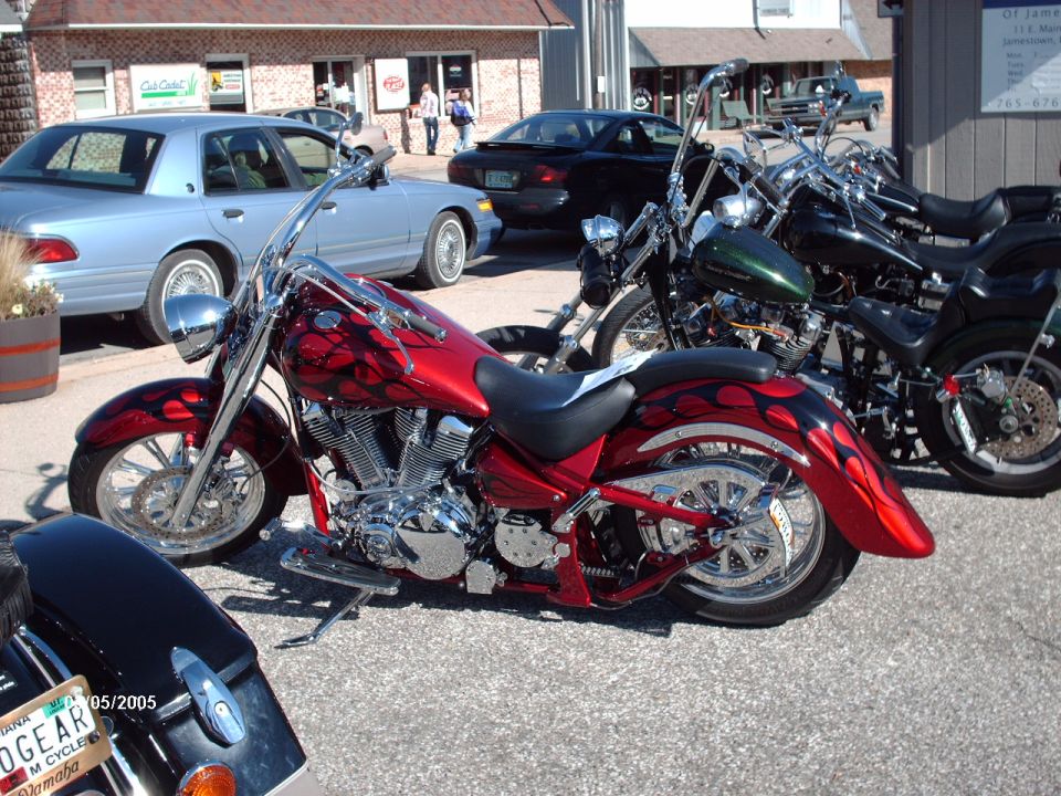 Custom red motorcycle with flame graphics parked next to other motorcycles and cars