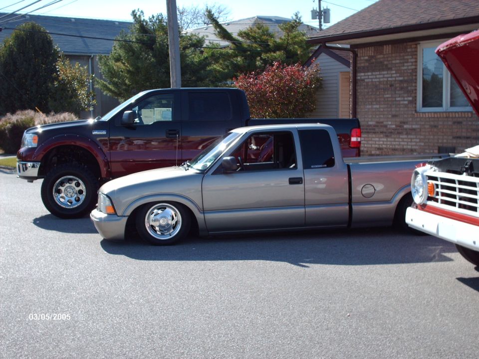 Silver pickup truck with chrome wheels, lowered suspension, parked next to a dark pickup truck and a red vehicle. Date stamp 03/05/2005