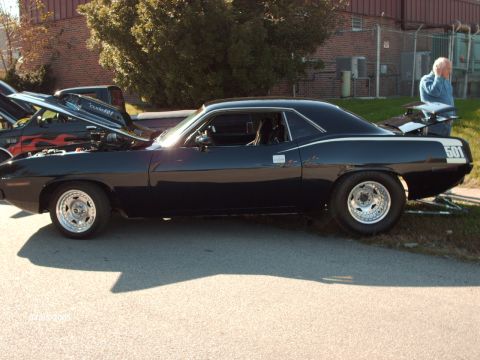 1995 Ford Probe - A black Plymouth Barracuda is displayed at a car show next to a truck with its hood open.