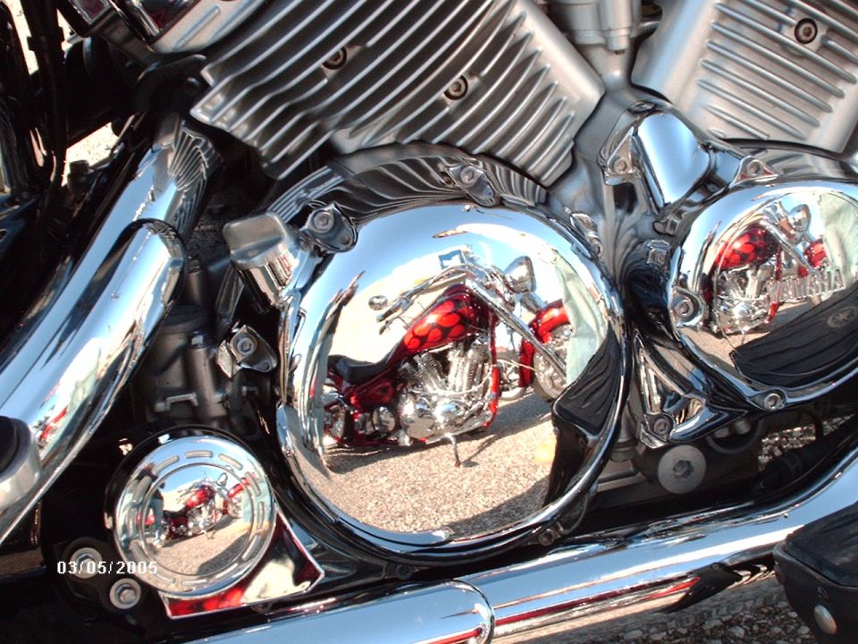 Chrome motorcycle engine with a reflection of a red motorcycle with flames