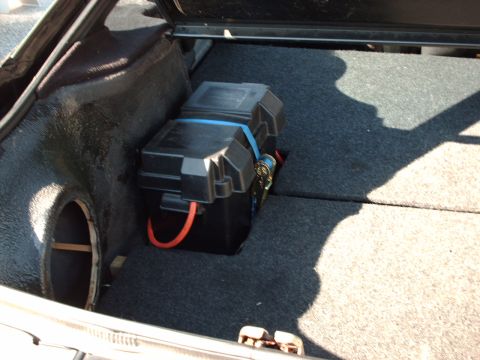 1995 Ford Probe - The trunk of a car contains a battery box with red cables, secured by a blue strap.