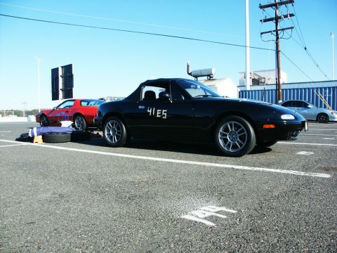 2001 Mercury Grand Marquis - A black convertible sports car with racing numbers is parked in a lot next to a red car.