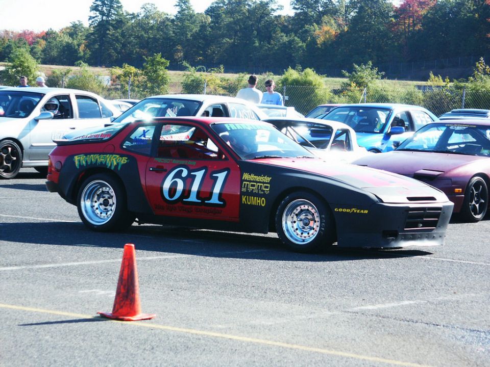 Red and black Porsche 944 with number 611 on the door, parked at a track with other cars