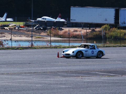 2001 Mercury Grand Marquis - A white sports car navigates a course marked by cones, with airplanes and a trailer in the background.