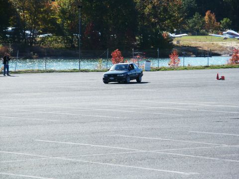 2001 Mercury Grand Marquis - A dark sedan drives on an asphalt lot with trees and water in the background.
