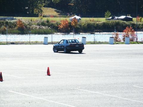 2001 Mercury Grand Marquis - A dark sedan with racing numbers is seen from the rear on a paved lot, with water and trees in the background.