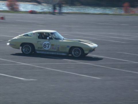 2001 Mercury Grand Marquis - A yellow 1965 Chevrolet Corvette races on a track, displaying the number 67.