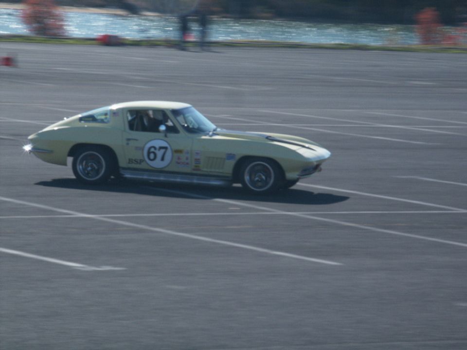 Yellow 1965 Chevrolet Corvette with racing number 67 on door, on asphalt track