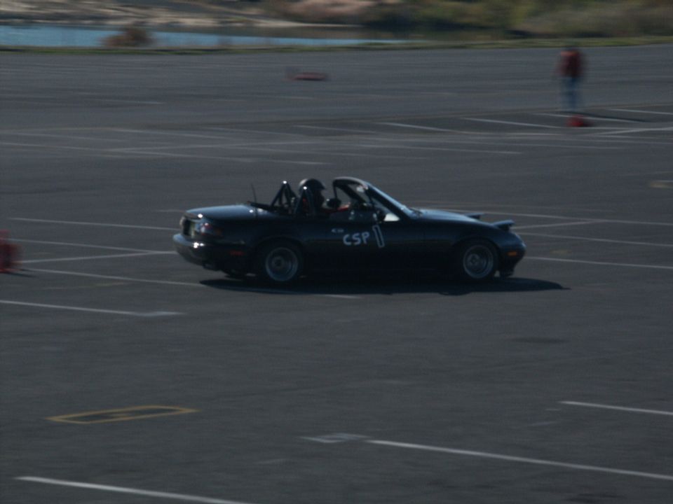 Black convertible sports car with roll bar, number 1, and 'CSP' on door, driving on asphalt track