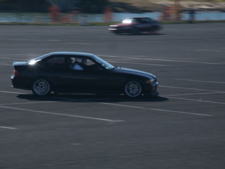 Black coupe driving on a paved surface with another car blurred in the background