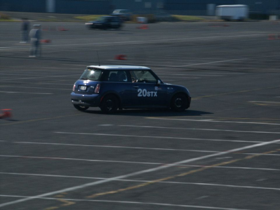 Blue Mini Cooper with "20STX" on the side driving on a paved track with orange cones