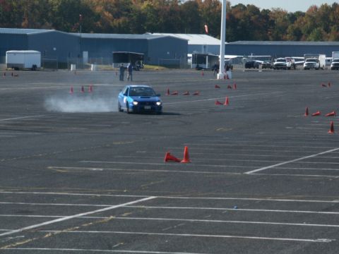 2001 Mercury Grand Marquis - A blue Subaru WRX STI drifts around a course marked by orange cones, kicking up tire smoke.