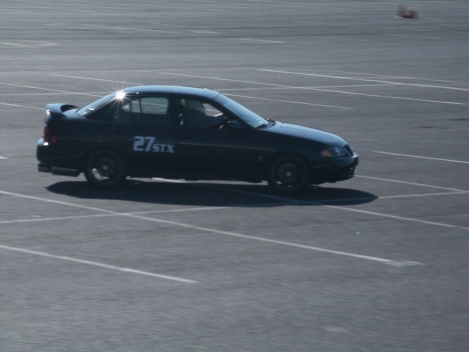 Black sedan with "27 STX" on the door, seen from the side on a paved lot