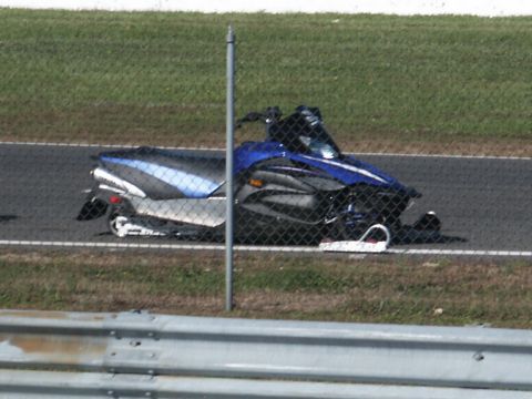 2001 Mercury Grand Marquis - A snowmobile is parked on a race track, partially obscured by a fence.