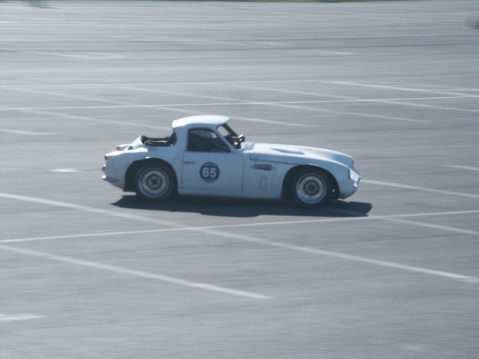 White sports car with blue circle and number 65 on the door, driving on a paved surface