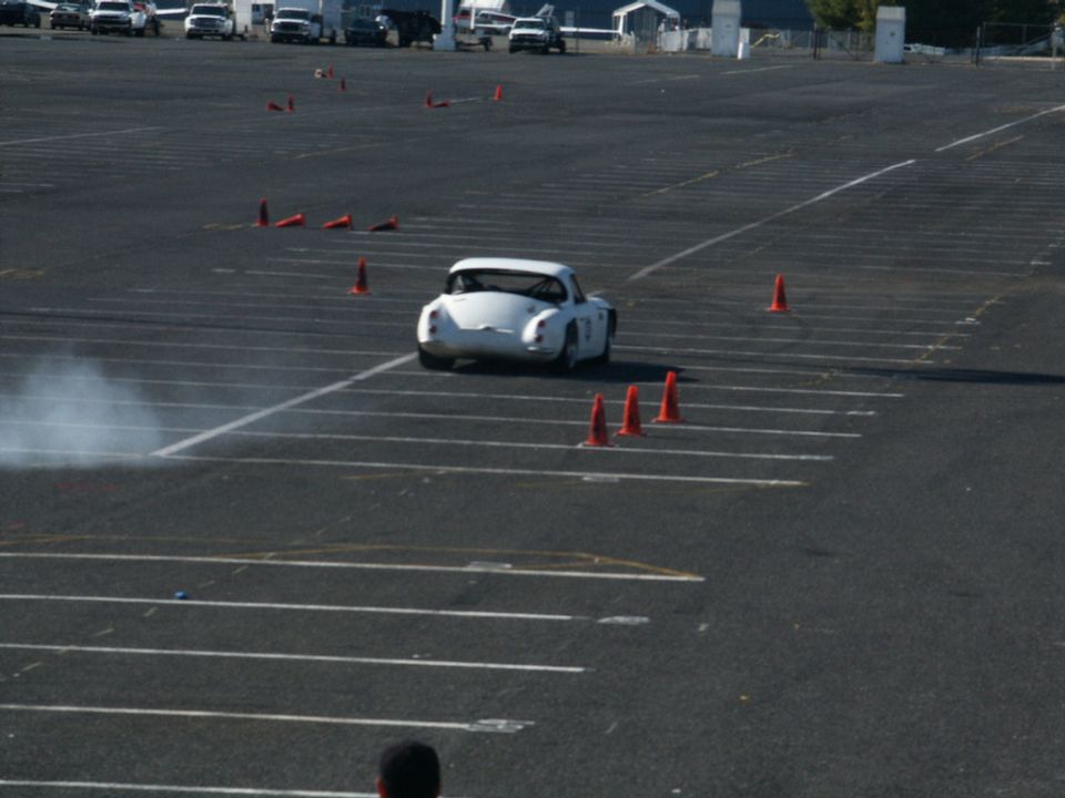 White sports car doing a maneuver on a paved lot with cones