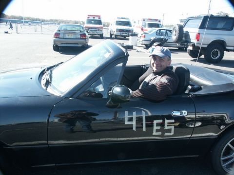 2001 Mercury Grand Marquis - A man sits in a black convertible with racing numbers on its side, parked at an event with other vehicles in the background.