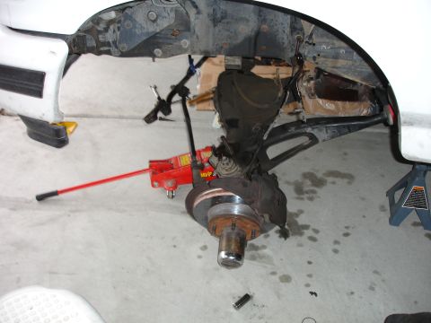 1996 Ford Bronco - The front wheel assembly is disassembled, showing the brake rotor and suspension linkage, supported by a jack.