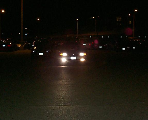 Dark car at night with headlights on facing camera in a parking lot