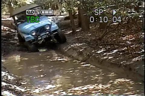 1989 Ford Bronco - Jeep CJ-7 navigates a muddy trail in a wooded area.