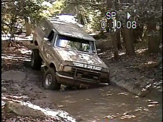 1989 Ford Bronco - This Ford Bronco navigates a muddy trail with trees on either side.