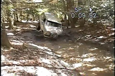 1989 Ford Bronco - A silver van navigates a muddy trail through a wooded area.
