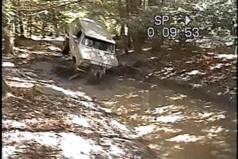 1989 Ford Bronco - An off-road vehicle navigates a muddy, wooded trail, appearing stuck in the mire.