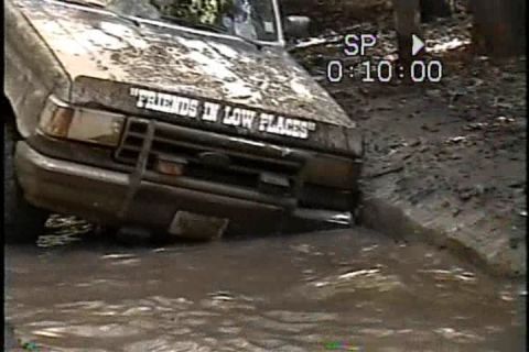 1989 Ford Bronco - This vehicle is stuck deep in the mud and water, with text on its hood.