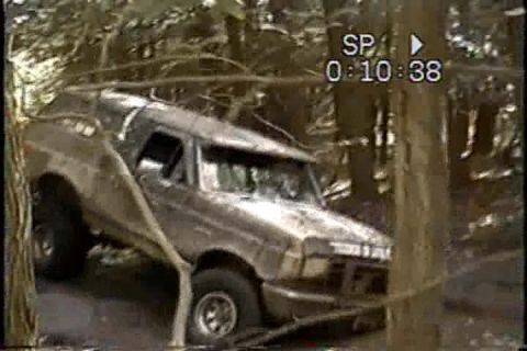 1989 Ford Bronco - This 1989 Ford Bronco is captured off-roading through a wooded area, showing its capability on challenging terrain.