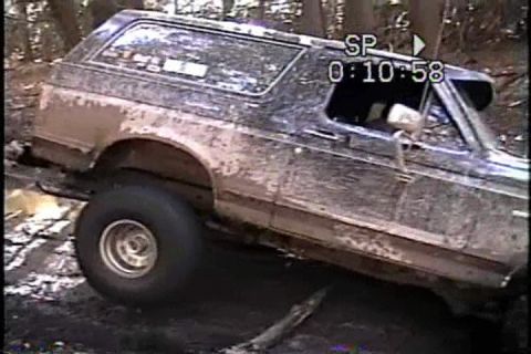 1989 Ford Bronco - Muddy 1989 Ford Bronco navigating a difficult off-road path through trees.