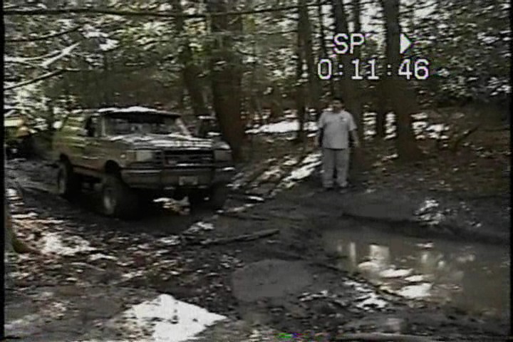 Brown Ford Bronco on a muddy trail, front-left view, lifted suspension