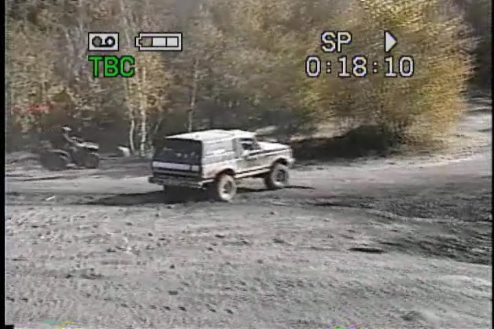 1989 Ford Bronco driving on a dirt road with an ATV in the background