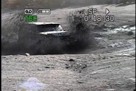 1989 Ford Bronco - A dark 1987 Ford Bronco navigates a muddy terrain, kicking up a significant amount of water and dirt.