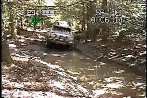 1989 Ford Bronco - An SUV navigates a muddy path through a dense forest, with another vehicle visible behind it.
