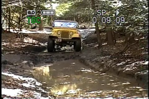 1989 Ford Bronco - A yellow Jeep navigates a challenging muddy off-road course.